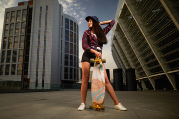 Plakat Beautiful sexy young girl in short shorts posing with skateboard in city on sunset background