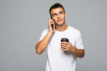 Portrait of happy man talking on phone and drinking coffee isolated on gray background