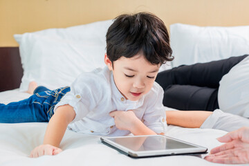Cute asian boy thinking in front of tablet. Distance learning online education. Cute asian boy doing homework on bed at home.