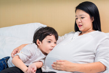 Fototapeta premium Sad little child, boy, hugging his Pregnant mother and Father on bed at home. Asian family