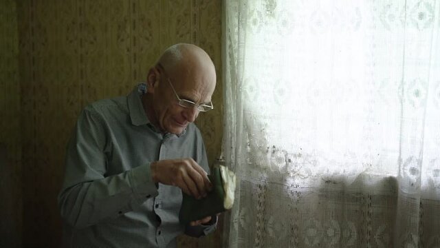 old man wearing eyeglasses reading old book sitting on sofa near window indoor
