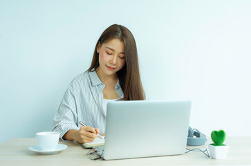 portrait a beautiful young woman taking notes and learning online with a laptop sitting in a table in the living room at the home office, work from home concept.