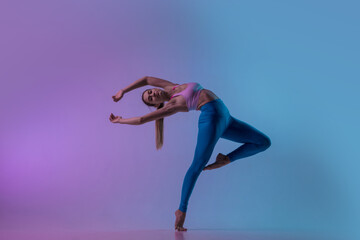 Graceful. Young sportive woman training isolated on gradient studio background in neon light. athletic and graceful. Modern sport, action, motion, youth concept. Beautiful caucasian woman practicing.