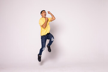 Young casual man celebrating his success and jumping over gray background.