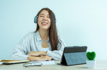 portrait of a beautiful Asian woman wearing headphones Laughing happily While chatting with colleagues On her desk At the home office, the idea of ​​working at home.