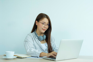 portrait of a beautiful Asian woman wearing glasses wears headphones Smile happily And look at the laptop While chatting online With colleagues On her desk At the home office, the idea of ​​working at