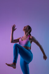 Fototapeta na wymiar Graceful. Young sportive woman training isolated on gradient studio background in neon light. athletic and graceful. Modern sport, action, motion, youth concept. Beautiful caucasian woman practicing.
