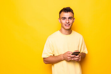 Young man holding smart phone in hands, using 3G internet, wi-fi, checking email, doing online shopping over yellow background