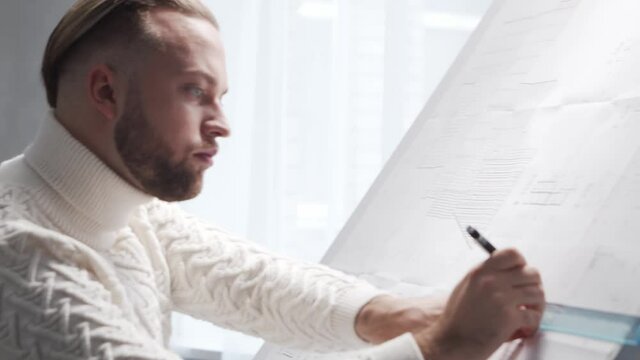 Concentrated architect works in loft using drawing board. Workplace of young engineer in modern office.