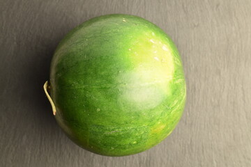 One ripe dark green organic watermelon, close-up, on a slate board.