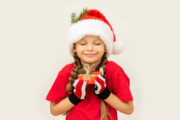 A little girl in a Christmas hat holds a gift in her hands.
