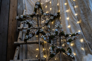Christmas country style decoration with lights of festive garland and rustic stars on wooden background, soft focus. 