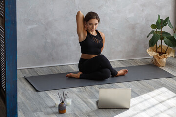 Young sporty female yoga instructor coaching online, making video of yoga lessons on laptop camera....