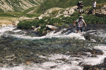 Tourists with ski poles cross the stormy mountain stream while traveling in the mountains