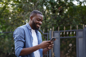 Happy man using mobile phone apps, texting message, browsing internet, looking at smartphone. Handsome Afro-American man using smartphone and smiling. Young people working with mobile devices.