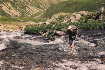 Young guy tourist is heavy with a backpack barefoot gets over river