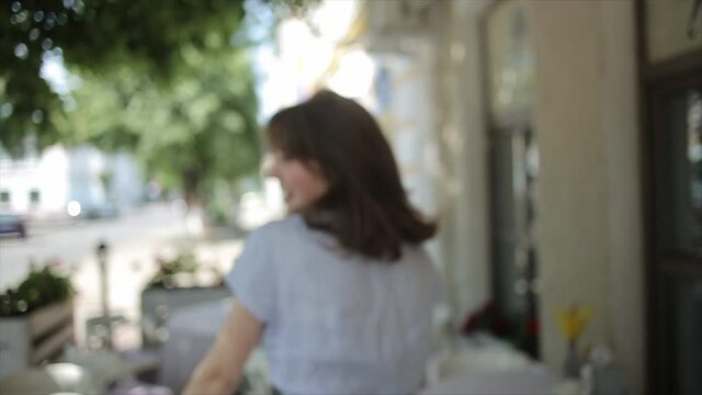 A charming young woman is goes between the tables of a summer cafe and smiling while turning to the camera. Medium shot. Slow motion