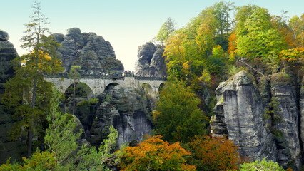 alte Basteibrücke mit Menschen im Nationalpark Sächsische Schweiz zwischen Felsen und Bäumen im Herbst