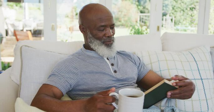 Senior african american man reading book and holding mug of tea