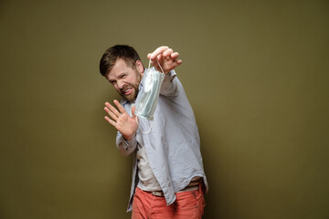 Squeamish, frightened man holds a used medical mask with two fingers and shows a stop gesture....