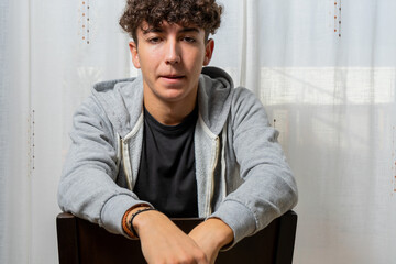 Attractive young man with curly hair wearing gray sweatshirt posing on white curtains background