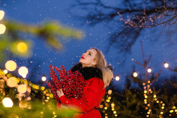 Obraz na płótnie Canvas Portrait of a woman posing with winter berries against Christmas lights.Snowing.