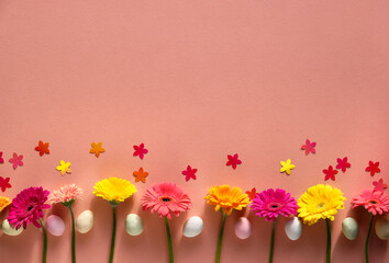 Easter creative border, top view. Marzipan Easter eggs, gerbera flowers, confetti on orange paper