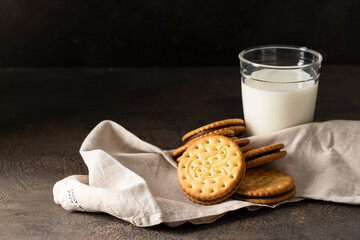 Sandwich biscuits cookies with chocolate filling with glass of milk on dark background for breakfast.