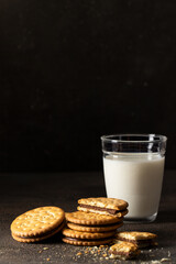 Sandwich biscuits cookies with chocolate filling with glass of milk on dark background for breakfast.