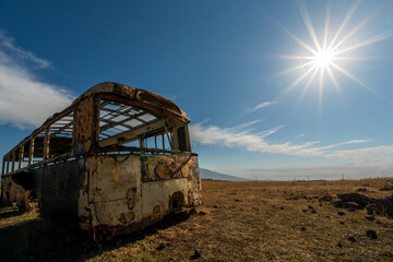 Fototapeta na wymiar An old wreck of a bus on a field in Armenian countryside. Transport infrastructure is in disrepair and often still from Soviet era. Provides interesting photo opportunities nevertheless.