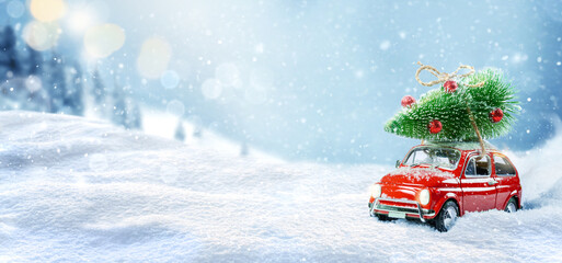 Retro toy car carrying christmas tree on roof in snowy winter forest. Christmas background. Holidays card.
