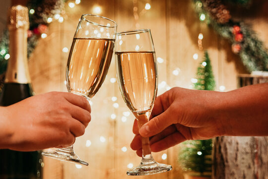 Two glasses of champagne are knocked by two women's hands on the background of Christmas decorations. New year with champagne. image with selective focus and tinting.
