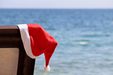 Christmas on a beach, New Year celebration on a sea coast. Santa hat on a lounge chair against the...