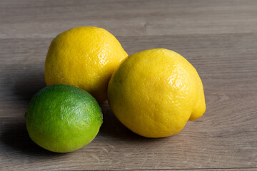 Two yellow lemons and a green lime on a wooden table