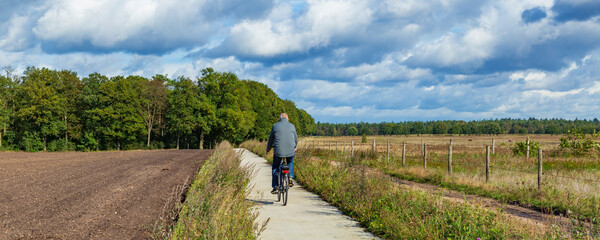 Man cycling between farm land with forest in the background in Gelderland in the Netherlands