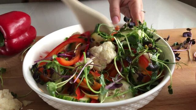 The girl mixes the ingredients of a vegetable salad in a plate