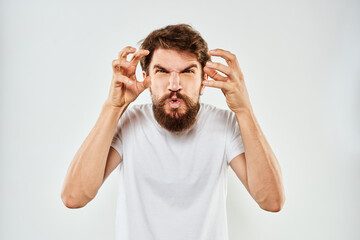 Naklejka premium Emotional bearded man in a white t-shirt gestures with his hands light background