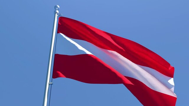 The national flag of Austria is flying in the wind against a blue sky