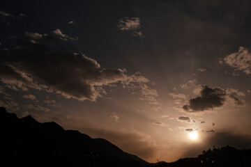 silhouette of mountains and city against the setting sun and clouds.