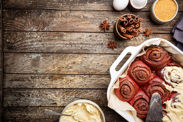 Homemade cinnamon rolls red velvet with cream cheese glaze on wooden background, top view