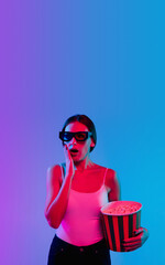 Shocked with popcorn. Young caucasian woman's portrait on gradient blue-purple studio background in neon light. Concept of youth, human emotions, facial expression, sales, ad. Flyer, cinema