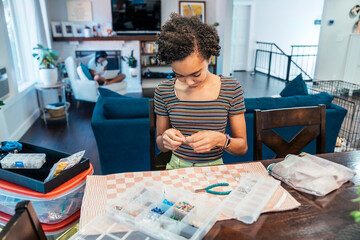 Fototapeta na wymiar Teen girl sitting at dining room table crafting jewelry