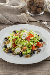 Fresh salad with feta cheese and walnuts on white plate on wooden table
