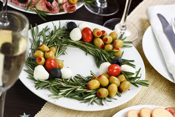 Fototapeta na wymiar An appetizer of rosemary stuffed with olives with baby mozzarella and cherry tomatoes. Made in the form of a Christmas wreath.
