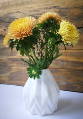 Bouquet of yellow orange autumn flowers, Asters, pleated white ceramic vase, old wooden boards texture background, white surface, decorating.