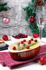 Chicken liver pate with butter topped with cranberry and rosemary served in the ceramic dish on the white table surrounded by Christmas attributes. Festive table setting