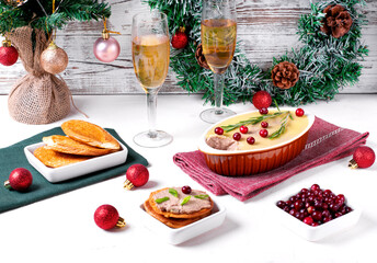 Chicken liver pate with butter topped with cranberry and rosemary served in the ceramic dish on the white table surrounded by Christmas attributes. Festive table setting