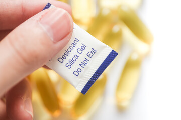 Hand holding a Desiccant Silica Gel Package on yellow Supplement Capsules