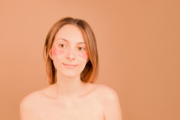 Obraz premium The concept of cosmetic skin care under the eyes. Girl with patches under the eyes on a brown background.