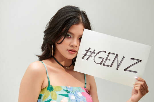 Trendy teenager show a text board with the text " gen z", she has rainbow eyeshadow and croptop tropical pattern